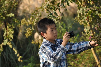 Teenage boy photographing plants at public park