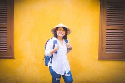 Portrait of smiling woman standing against yellow wall