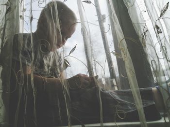 Close-up of young woman standing in curtain at home