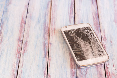 Mobile smartphone with broken screen on wooden table or office desk background with copy space 