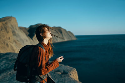 Woman standing on rock by sea against sky