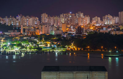 Illuminated buildings by river against sky at night