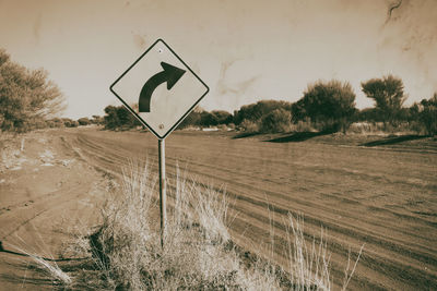 Road sign on street by field against sky