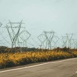 Road by electricity pylon against sky