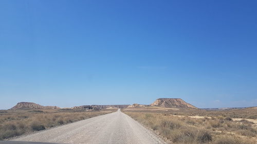 Road amidst desert against clear blue sky