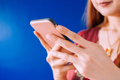 Midsection of woman using mobile phone against blue sky