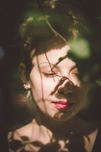 Close-up of young woman with eyes closed by branches during sunlight