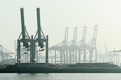 Cranes at harbor against clear sky