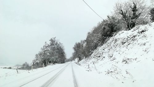 Snow covered road amidst trees against sky