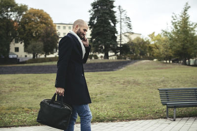 Side view of mid adult businessman talking on mobile phone while walking on sidewalk