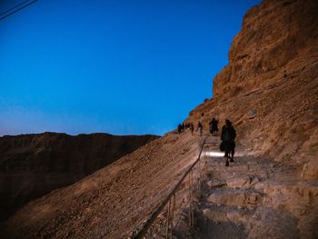 People walking on mountain against clear blue sky