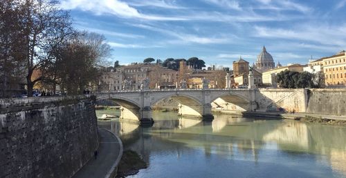 Bridge over river by buildings in city against sky