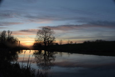 Silhouette trees by lake against sky during sunset