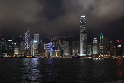 Illuminated skyscrapers at victoria harbour against sky at night