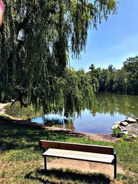 Empty bench by lake against sky