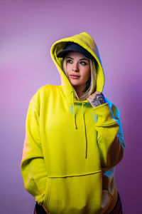 Portrait of young woman standing against yellow background