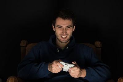 Man playing video game while sitting against black background