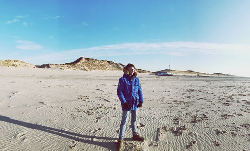 Full length of teenage boy standing on sand at beach against sky during sunny day