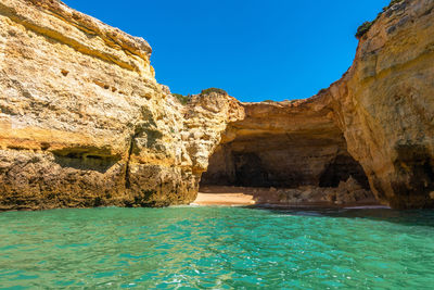 Rock formations by sea against clear blue sky