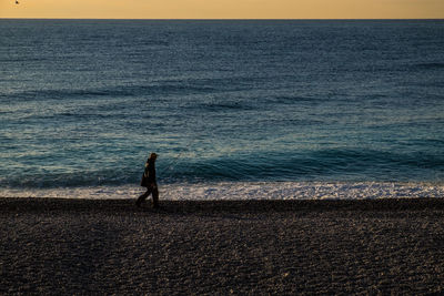 Side view of a silhouette man walking on calm beach