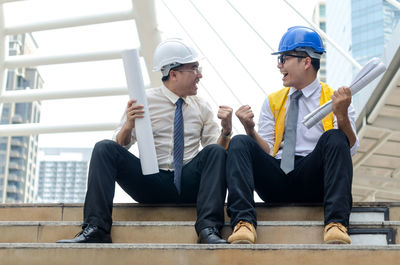 Male engineers clenching fists while sitting on steps