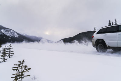 Off-road vehicle moving on snow covered field against cloudy sky