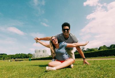 Happy young woman with arms raised on field against sky