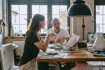 Entrepreneur explaining female colleague while holding photograph at table in studio