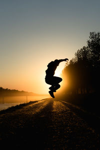 Silhouette man jumping on tree against sky during sunset