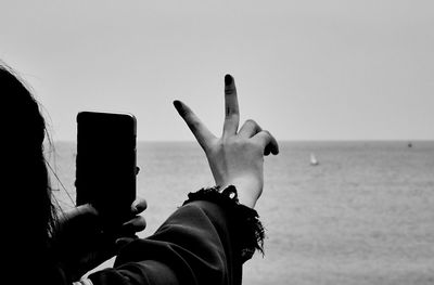 Close-up of woman photographing while gesturing peace sign at beach