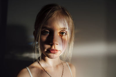 Close-up portrait of girl standing against wall at home