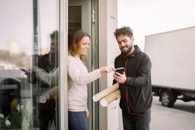 Female customer signing on smart phone while receiving package from delivery man