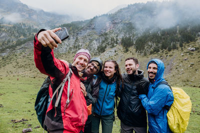 Happy friends hikers with backpacks taking selfie with smart phone on mountain. boys and girls smile