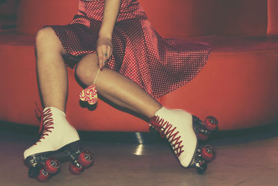 Low section of woman wearing roller skates and holding lollipop while sitting on sofa