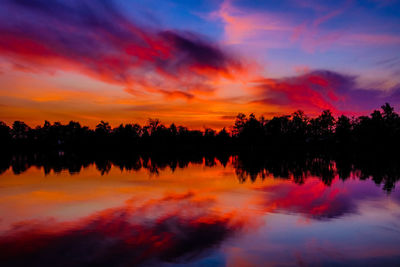 Silhouette trees on landscape against dramatic sky during sunset