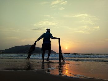 Rear view of silhouette fisherman holding nets while walking at shore during sunset