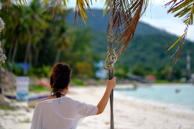 Rear view of woman sitting on rope swing at beach