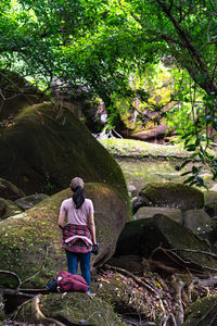 Rear view of woman standing by rocks in forest