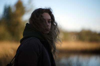 Side view of young woman standing against lake