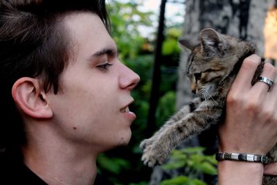 Side view of young man playing with cat in forest