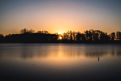 Silhouette trees by lake against sky during sunset