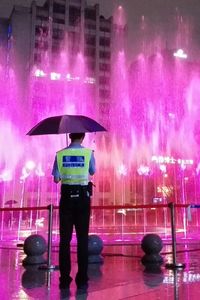 Rear view of woman holding umbrella at night