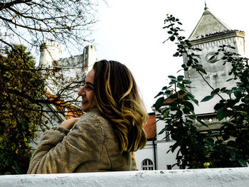 Low angle view of woman standing by bare tree against clear sky