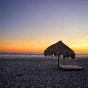Thatched roof parasol at beach against sky during sunset