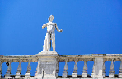 Low angle view of statue on railing against clear blue sky