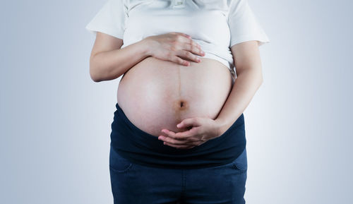 Midsection of woman touching face against white background
