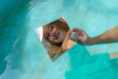 Young woman holding mirror with reflection in wading pool