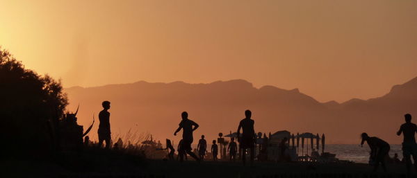 Silhouette people on beach against clear sky during sunset