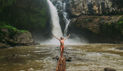 Young woman standing against waterfall