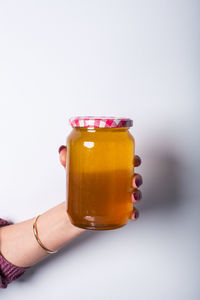 Close-up of woman hand holding glass jar against white background